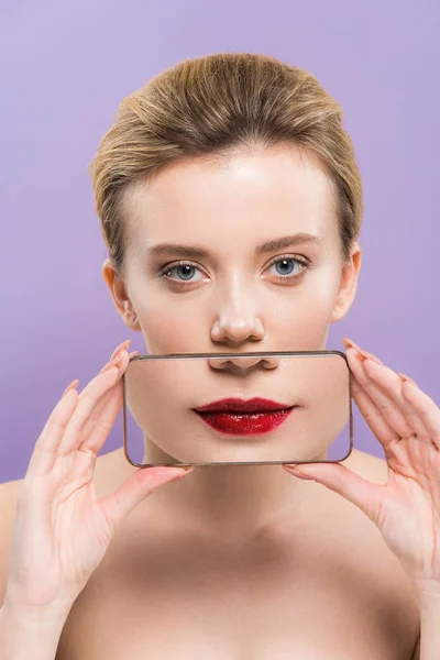 Attractive naked woman covering mouth with smartphone with lips on screen isolated on purple — Stock Photo