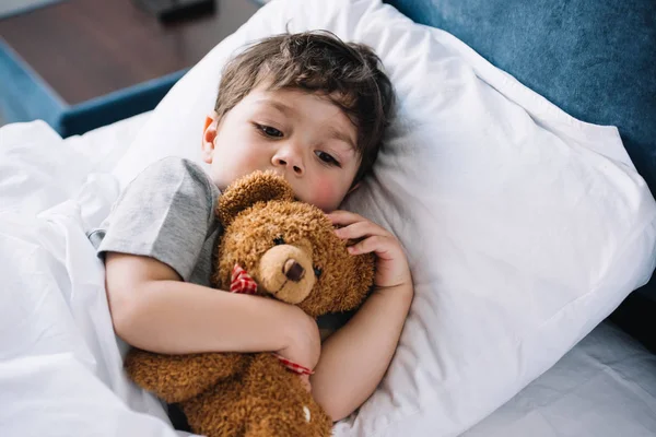 Cute kid lying in bed with teddy bear at home — Stock Photo