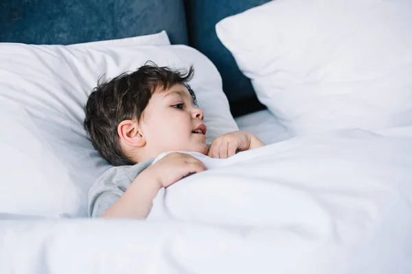 Cute kid lying on white pillow in bed at home — Stock Photo