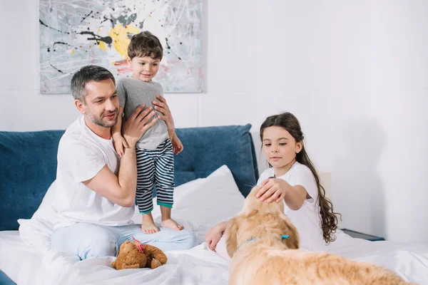 Alegre padre celebración en brazos lindo niño y mirando a mascota cerca de hija - foto de stock