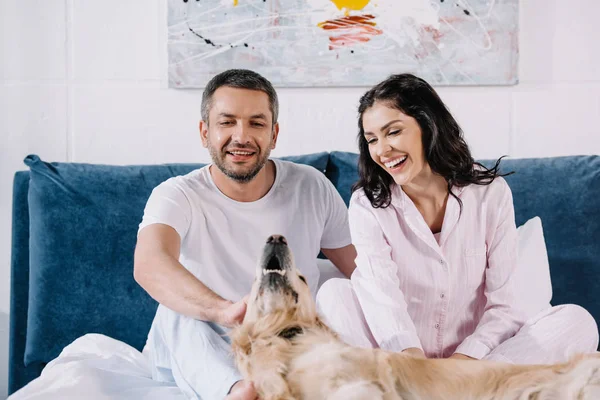 Selective focus of cheerful man and woman near cute golden retriever in bedroom — Stock Photo