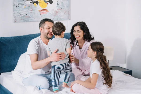 Padres felices mirando al hijo pequeño cerca de la hija sonriente - foto de stock