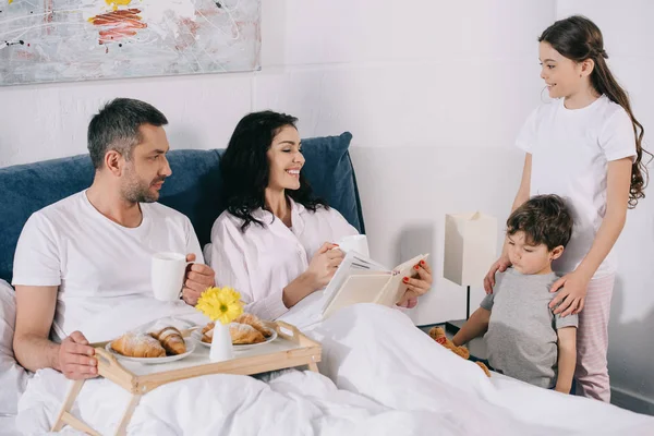 Счастливые дети смотрят на веселую маму рядом с отцом в постели — стоковое фото