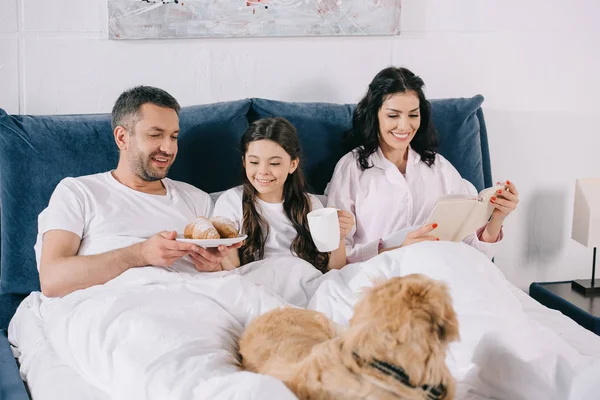 Enfoque selectivo de la mujer feliz libro de lectura cerca de marido, hija y perro - foto de stock