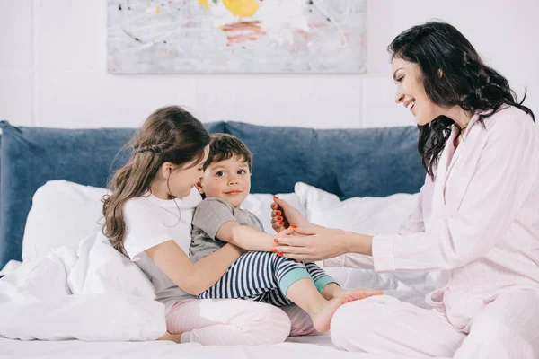 Happy mother touching cheerful toddler son near cute daughter in bedroom — Stock Photo