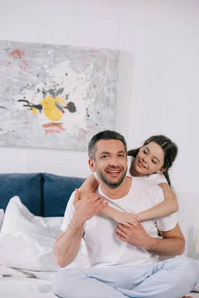 Feliz hija abrazando alegre padre en el dormitorio - foto de stock