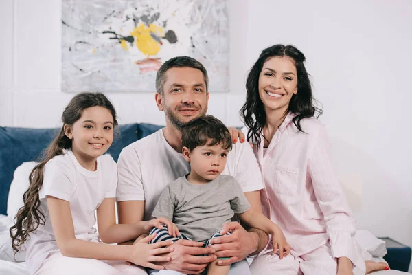 Fröhliche Eltern lächeln neben glücklichen niedlichen Kindern im Schlafzimmer — Stockfoto