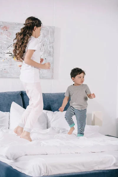 Cute child jumping on bed with adorable toddler brother — Stock Photo