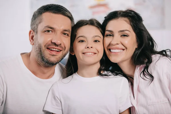 Enfant heureux souriant près des parents gais et regardant la caméra — Photo de stock