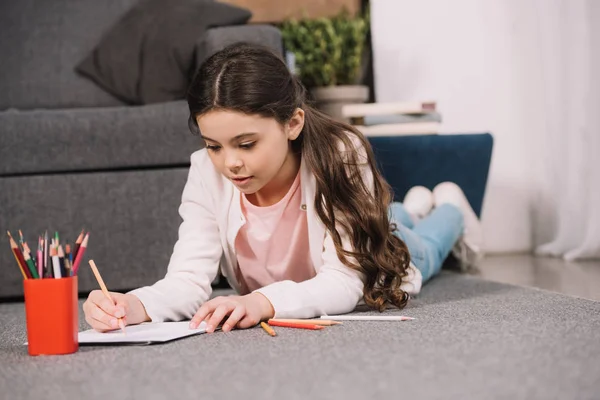 Selective focus of cute kid lying on floor and drawing on paper in living room — Stock Photo