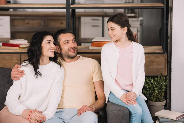 Niño feliz mirando a padres alegres sentados en el sofá - foto de stock