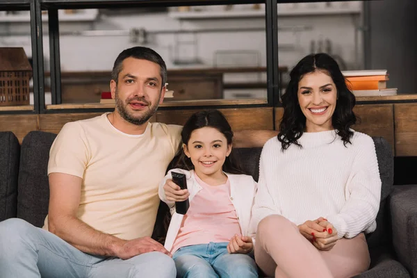 Bambino felice che tiene il telecomando mentre guarda il film con i genitori — Foto stock