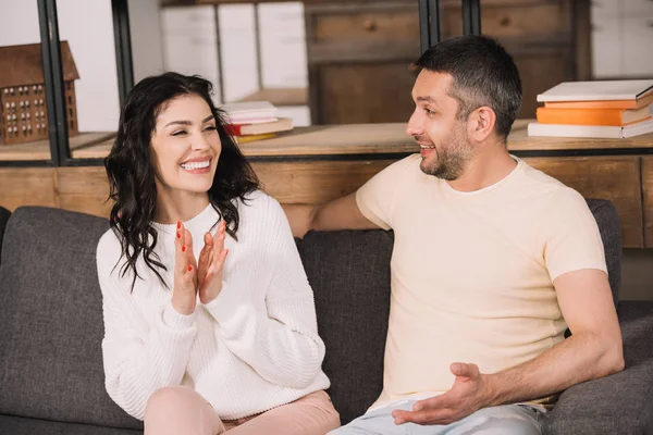 Happy man looking at cheerful brunette woman clapping hands at home — Stock Photo