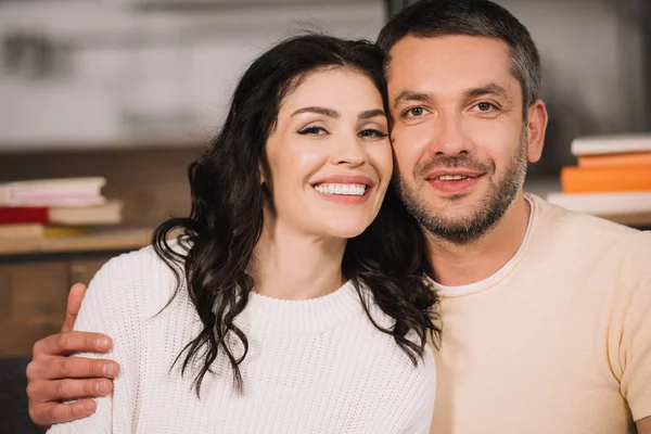 Hombre feliz abrazando mujer atractiva y alegre en casa - foto de stock