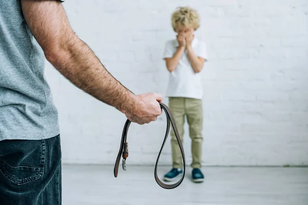 Cropped view of father with belt and crying son at home — Stock Photo