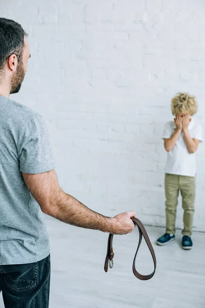 Cropped view of father with belt and crying son at home — Stock Photo