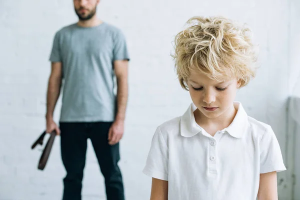 Vista recortada del padre con cinturón y el hijo molesto en casa - foto de stock