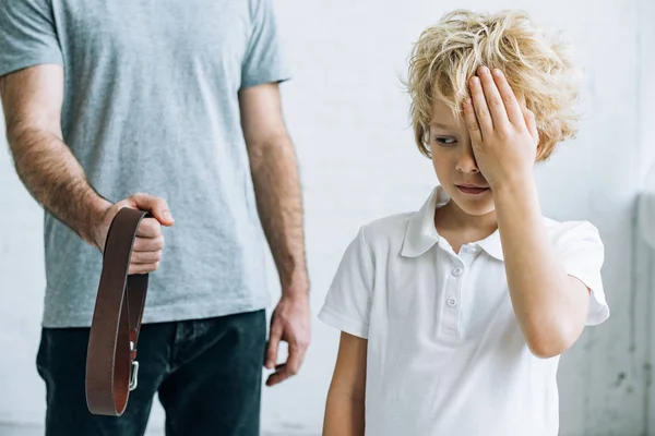 Cropped view of father with belt and upset son at home — Stock Photo