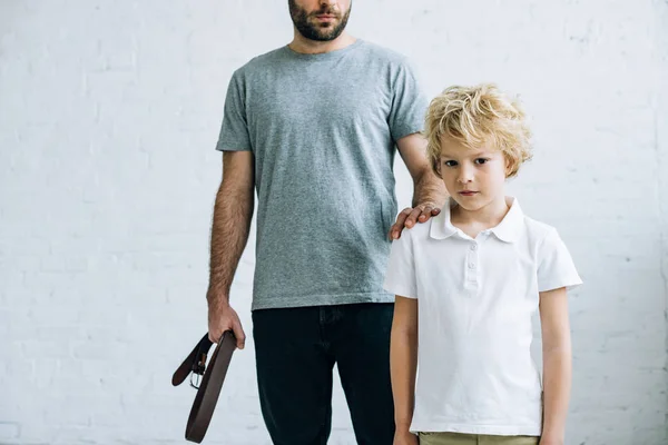 Cropped view of father with belt and upset son at home — Stock Photo