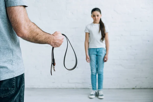Cropped view of father holding belt and upset daughter at home — Stock Photo