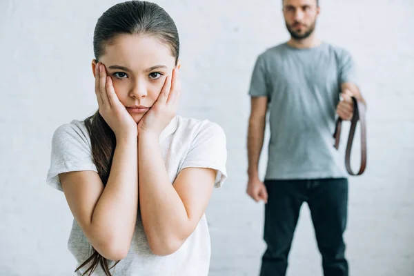 Cropped view of father holding belt and upset daughter at home — Stock Photo