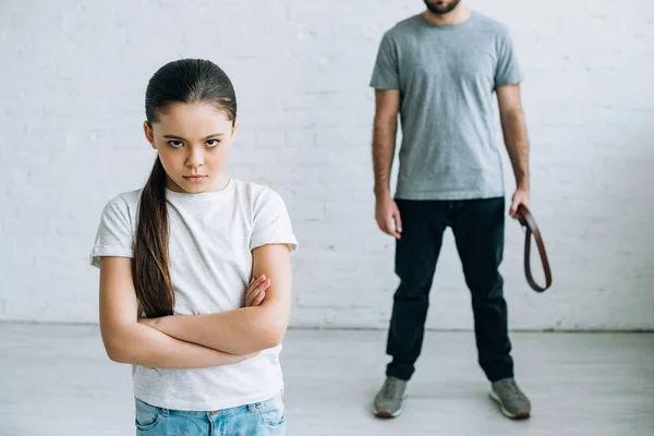 Cropped view of father holding belt and upset daughter at home — Stock Photo