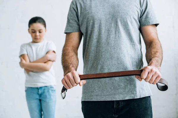 Visão cortada do pai segurando cinto e filha chateada em casa — Fotografia de Stock