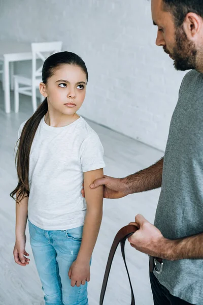 Partial view of father with belt in hand grabbing daughter at home — Stock Photo