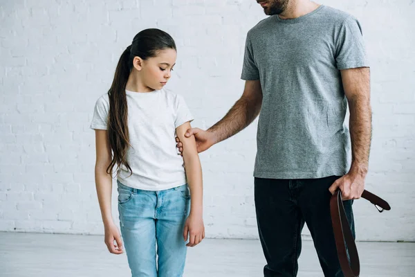 Partial view of father with belt in hand grabbing daughter at home — Stock Photo