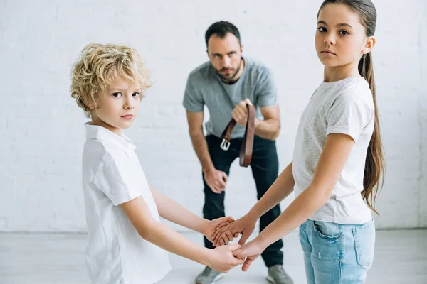 Abusive father holding belt and children holding hands at home — Stock Photo