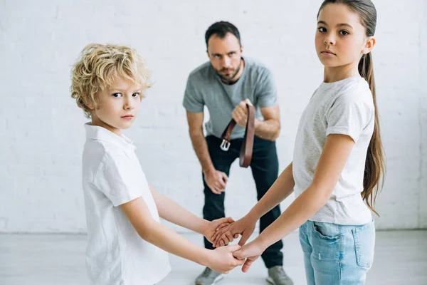 Padre abusivo che tiene la cintura e i bambini che si tengono per mano a casa — Foto stock