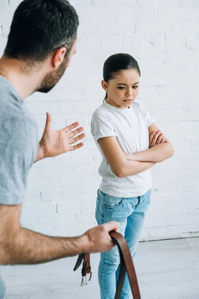 Partial view of father holding belt and scolding upset daughter at home — Stock Photo