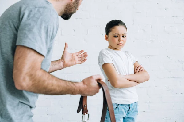 Partial view of father holding belt and scolding upset daughter at home — Stock Photo