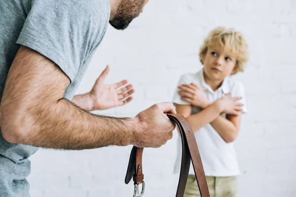 Cropped view of father holding belt and scolding son at home — Stock Photo