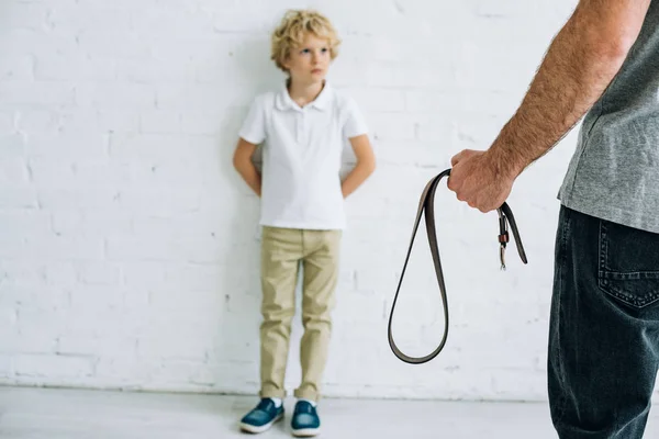 Cropped view of father holding belt and son having conflict — Stock Photo