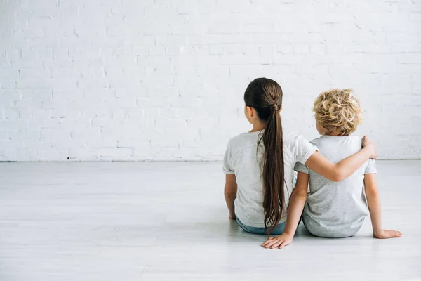 Rückansicht von zwei Kindern, die sich zu Hause auf dem Boden umarmen — Stockfoto