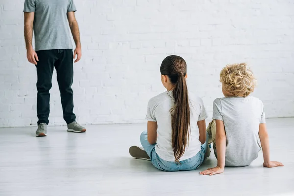 Partial view of abusive father and sad kids sitting on floor — Stock Photo