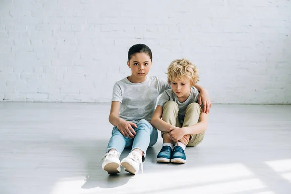 Triste sœur assise sur le sol et embrassant frère — Photo de stock