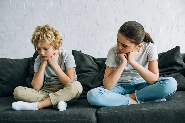 Двое грустных детей сидят на диване в гостиной — стоковое фото
