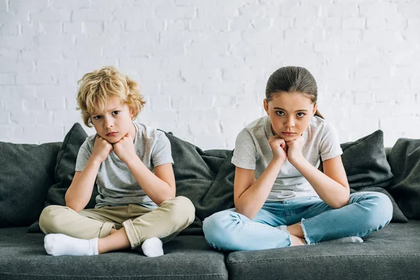 Dos niños tristes sentados en el sofá en la sala de estar - foto de stock