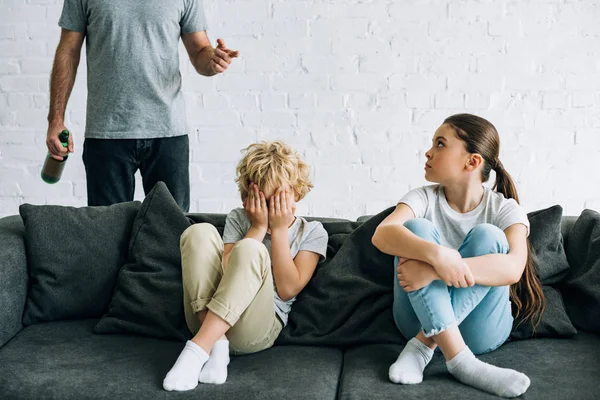 Cropped view of alcohol addicted father with beer and upset children on sofa — Stock Photo