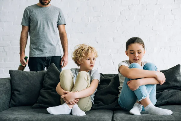 Vue recadrée du père alcoolique accro à la bière et bouleversé les enfants sur le canapé — Photo de stock