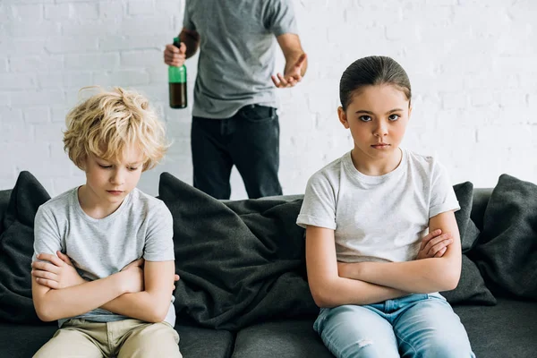 Cropped view of alcohol addicted father with beer and upset children on sofa — Stock Photo