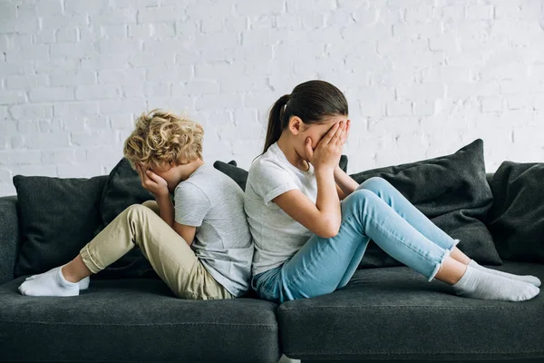 Dos niños tristes sentados en el sofá en la sala de estar - foto de stock