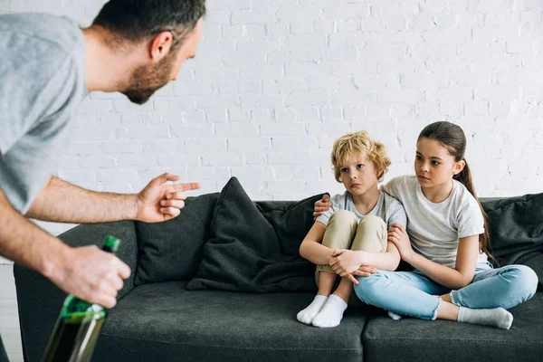 Vista recortada de padre adicto al alcohol con cerveza y niños molestos en el sofá - foto de stock