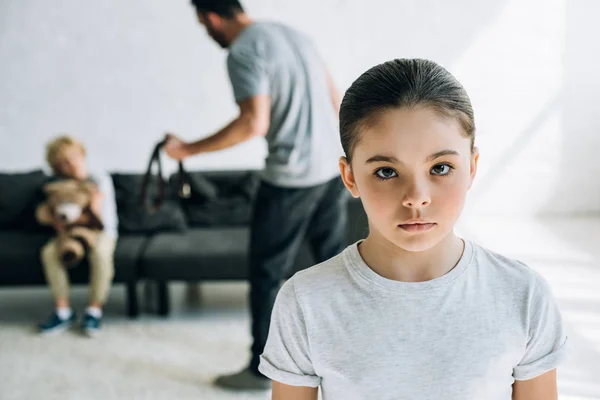 Hijos tristes y padre abusivo sosteniendo el cinturón en casa - foto de stock