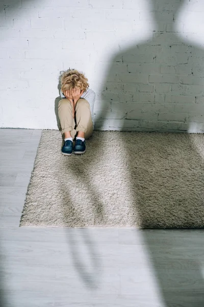 Силует і наляканий маленький хлопчик сидить на килимі — стокове фото