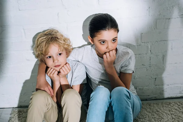 Scared sister embracing brother while sitting on carpet — Stock Photo