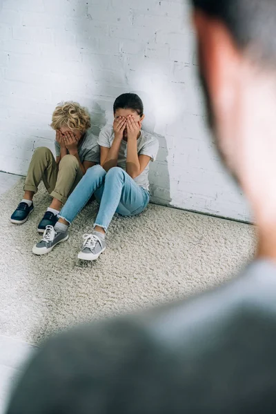 Vue recadrée du père et des enfants effrayés assis sur le tapis — Photo de stock