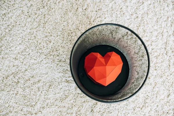 Red heart in black trash can on carpet — Stock Photo